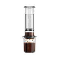 The Pull & Pour Shop AeroPress Clear XL coffee maker with a transparent Tritan chamber brewing coffee into a carafe.
