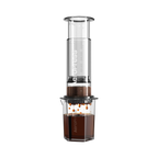 The Pull & Pour Shop AeroPress Clear XL coffee maker with a transparent Tritan chamber brewing coffee into a carafe.